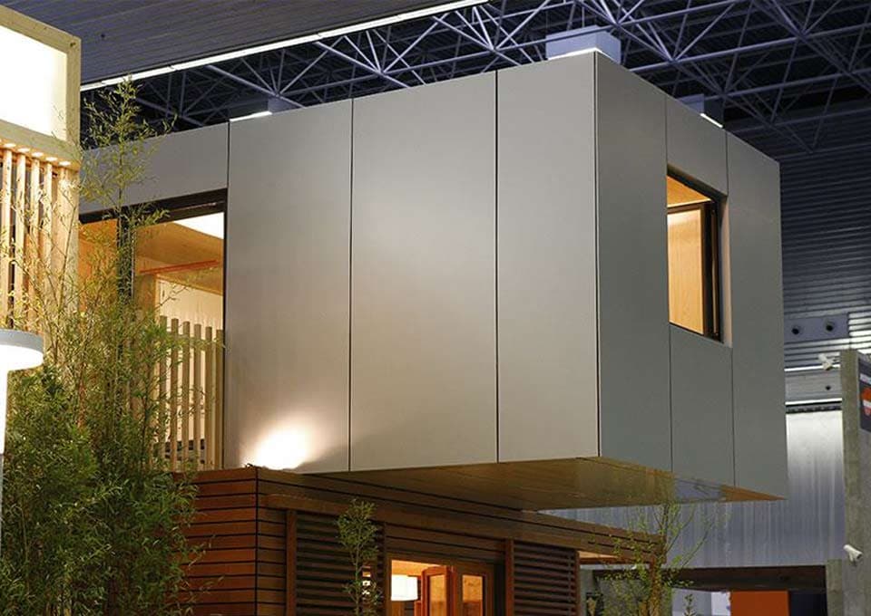 Volume architectural habillé de panneaux composites aluminium gris à joints creux, sur un stand d'exposition.